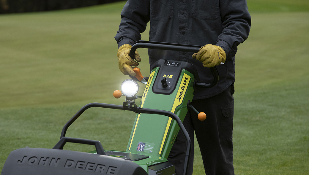 Close-up view of a person operating the 185 E-Cut Electric Walk Greens mower on a green golf course