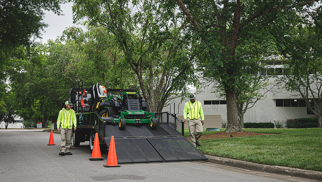 Two people loading a mower onto a trailer